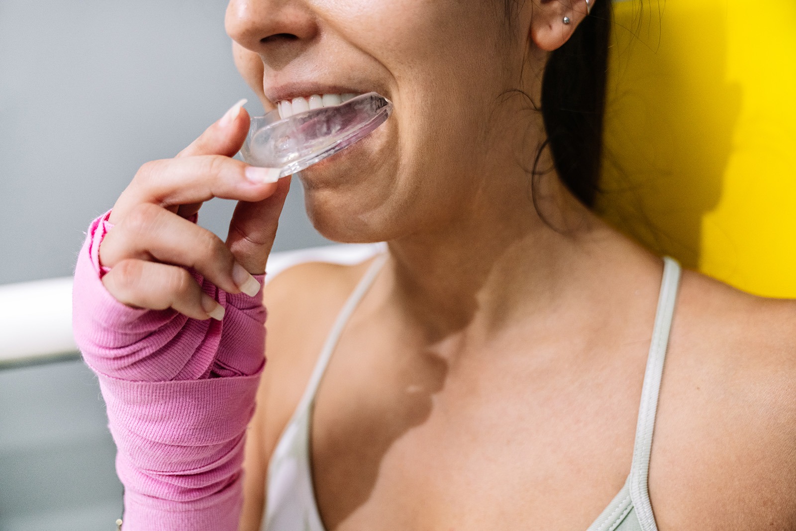 A smiling adult woman is shown in a waist-up shot, inserting a clear mouth guard in her mouth